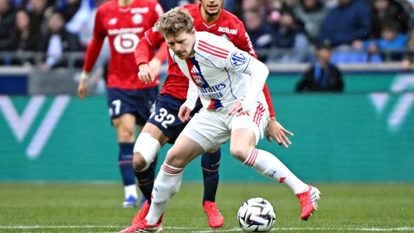 Un joueur en maillot blanc contrôlant le ballon sous la pression de deux adversaires en rouge.