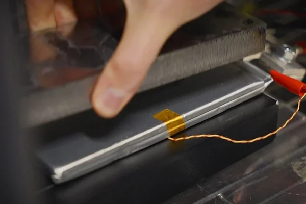 Une main appuie sur un composant métallique connecté par des fils sur une surface sombre