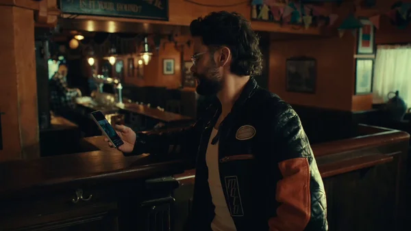 LeBouseuh dans un bar, smartphone en main, dans le cadre du tournoi de fléchettes entre créateurs