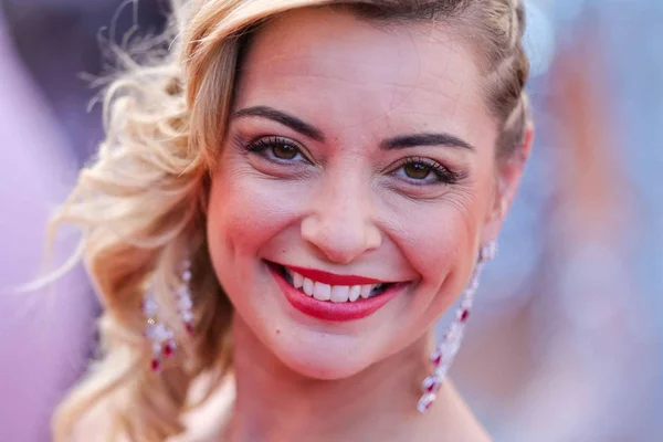 Priscilla Betti en gros plan, portant du rouge à lèvres rouge et des boucles d'oreilles.