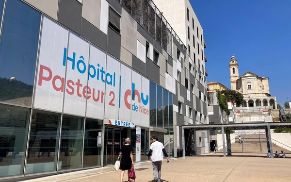 Deux personnes passant devant l'entrée vitrée de l'Hôpital Pasteur 2 à Nice