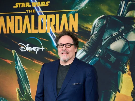 Jon Favreau, créateur de The Mandalorian, lors d'un événement promotionnel devant un fond officiel de la série Disney+.