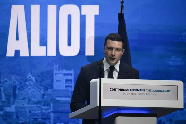 Vue d'une meeting à Perpignan le 28 février 2026 avec un orateur devant la banderole Continuons ensemble avec Louis Aliot