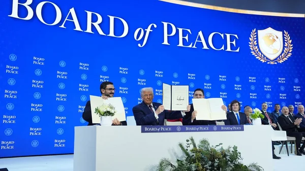 Groupe d'hommes levant des documents devant une bannière 'BOARD of PEACE' à Davos.