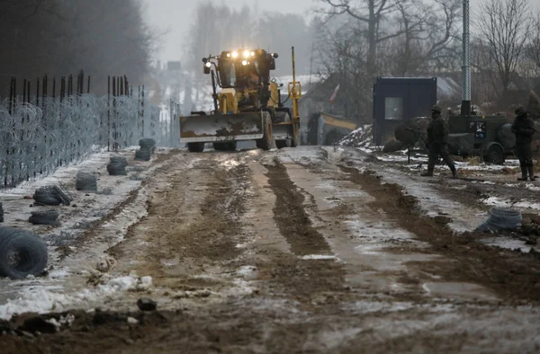 Un bulldozer sur une route boueuse bordée de barbelés et de matériaux de construction.