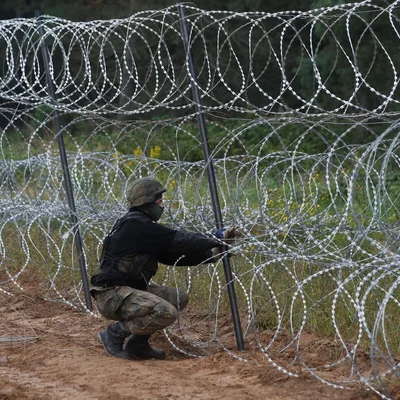 Un soldat en uniforme de camouflage installe des barbelés concertina.