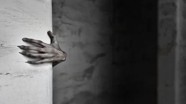 Main pâle aux ongles longs agrippant un mur