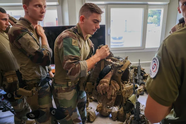 Des militaires en treillis s'affairent à ajuster leur équipement tactique dans un environnement intérieur.