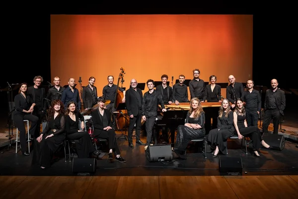 Un ensemble musical en tenue formelle posant sur scène avec divers instruments lors d'un événement à Toulouse.