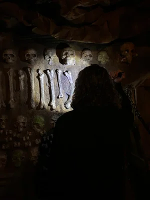 Une personne éclaire une accumulation de crânes et d'os dans l'obscurité.