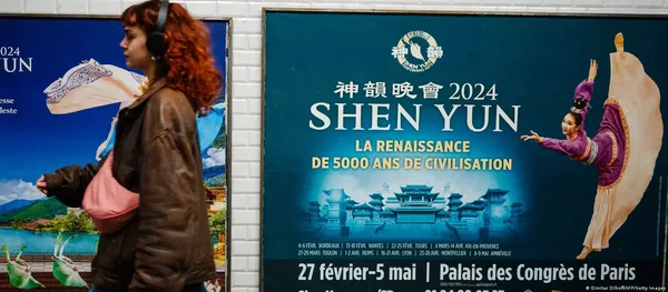 Un groupe de danseurs en costumes turquoise et rose performe avec des rubans devant un décor architectural doré.