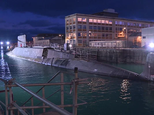 Un sous-marin dans le port de Cherbourg la nuit, entouré d'infrastructures éclairées.