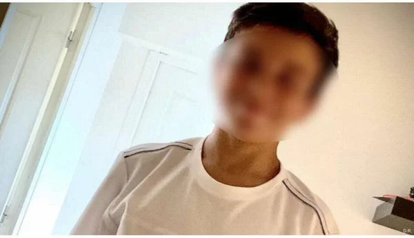 Une personne au visage flouté se tient près d'une porte blanche, portant un t-shirt à rayures.