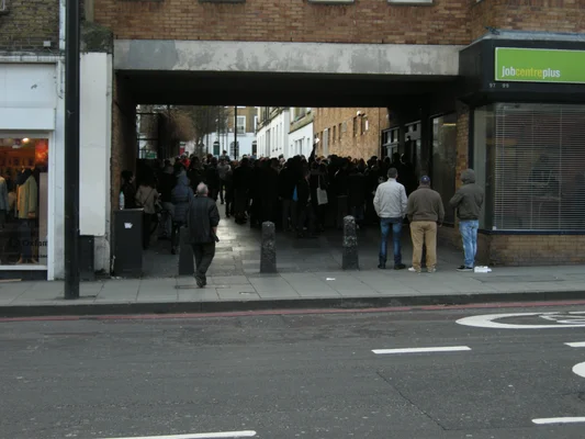 Une foule se rassemble sous une arcade de briques, devant un bâtiment Jobcentre Plus.