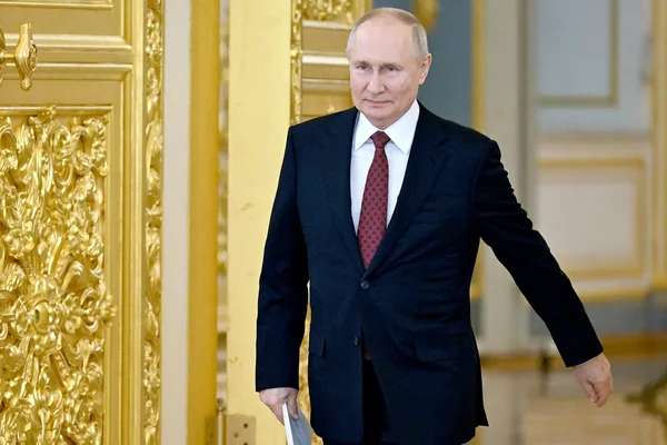 Vladimir Poutine tenant un document dans une salle décorée de panneaux dorés.