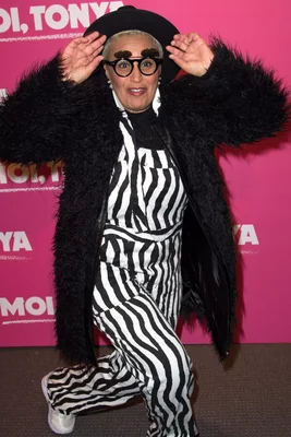 Lââm en manteau de fourrure noire posant sur un fond rose.