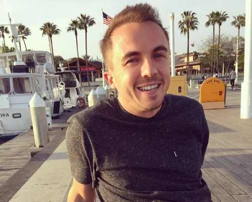 Frankie Muniz posant souriant sur un ponton près de bateaux.