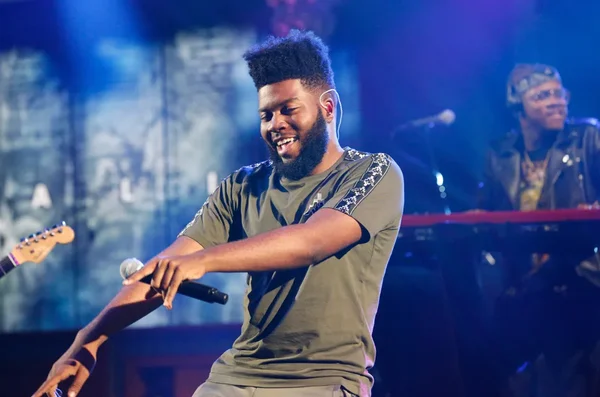 Khalid sur scène lors d'une performance live, vêtu d'un t-shirt olive.