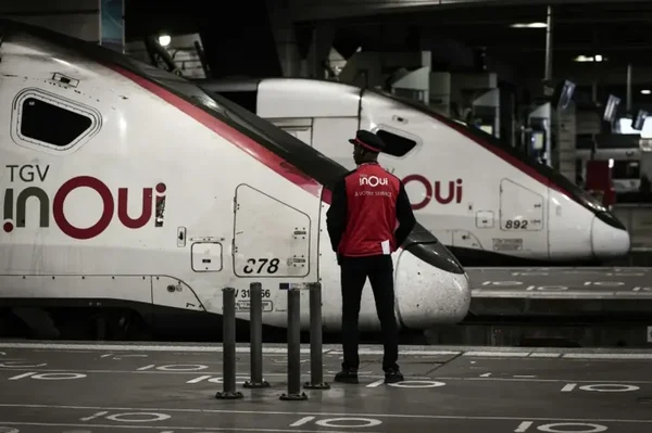 Deux trains TGV inOui en gare la nuit avec une personne en gilet rouge entre eux.