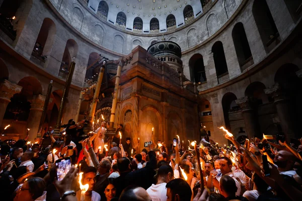 Foule avec des bougies allumées et des téléphones dans la basilique du Saint-Sépulcre lors d'une cérémonie.