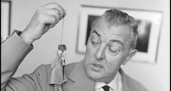Jacques Tati en costume tenant une figurine sur une ficelle, le nez en gros plan.