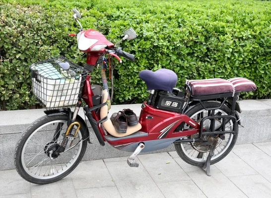 Un scooter électrique chinois rouge et gris garé sur une surface pavée.