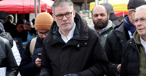 Scène de campagne ou de rassemblement public avec des militants et des tentes du parti socialiste en arrière-plan.