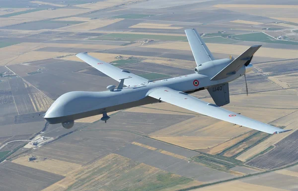 Un drone MQ-9 Reaper volant sur un patchwork de champs agricoles.