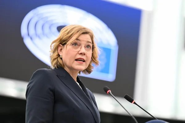 Intervenante à lunettes devant un podium avec microphones et graphique.