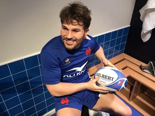 Figure de cire d'Antoine Dupont dévoilée en 2023 dans un vestiaire, tenant un ballon de rugby.