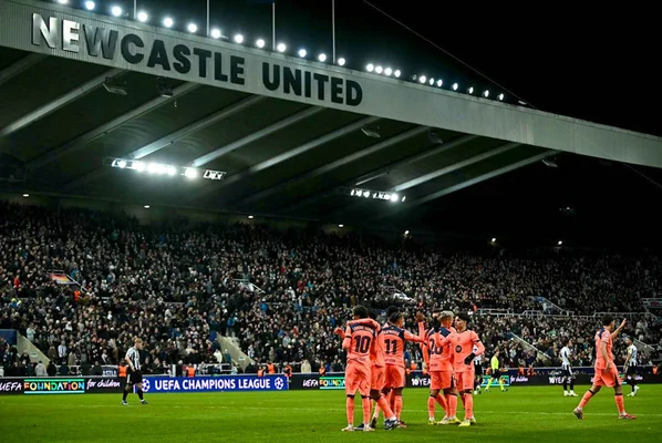 Célébration de joueurs en maillot rose sur la pelouse du stade de Newcastle, identifiable grâce à la signalétique UEFA Champions League.