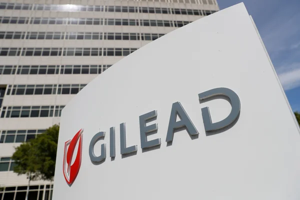 Panneau blanc avec le logo Gilead Sciences situé devant un grand immeuble de bureaux moderne.