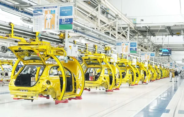 Ligne de production dans une usine Stellantis avec des carrosseries de véhicules et des ouvriers au travail.