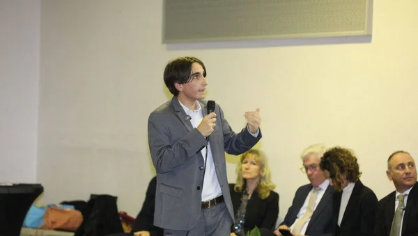 Ewan Corinaldesi s'exprimant au micro devant un public lors d'une réunion.