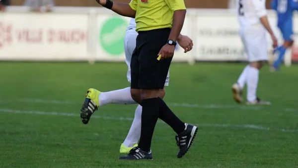 Un arbitre tenant un carton jaune sur un terrain de football.