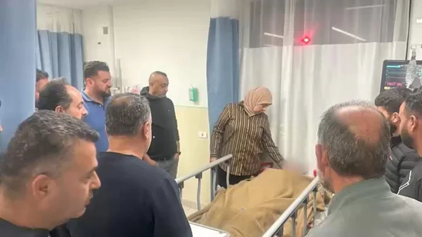 Un groupe de personnes se tient autour d'un lit d'hôpital, des rideaux bleus et du matériel médical visibles