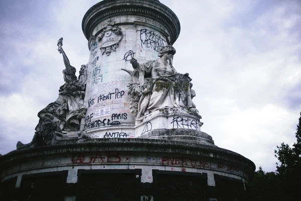 Le monument aux inscriptions politiques « VOTE FRONT POP » et « ANTIFA » sous un ciel nuageux.