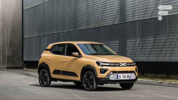 La Dacia Spring beige avec accents noirs stationnée devant une façade métallique industrielle moderne.