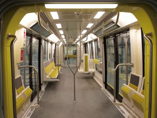 Vue de l'intérieur d'une rame de métro moderne avec ses sièges jaunes et gris et son allée centrale.