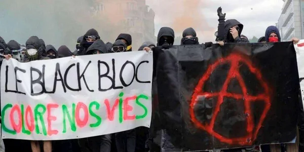 Des manifestants en black bloc tenant des banderoles anarchistes et revendicatives.
