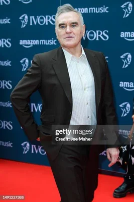 Morrissey standing on a red carpet with a blue backdrop featuring Ivors and amazon music logos.