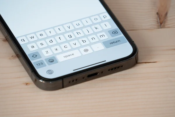 Un iPhone posé sur une table en bois montrant le clavier à l'écran.