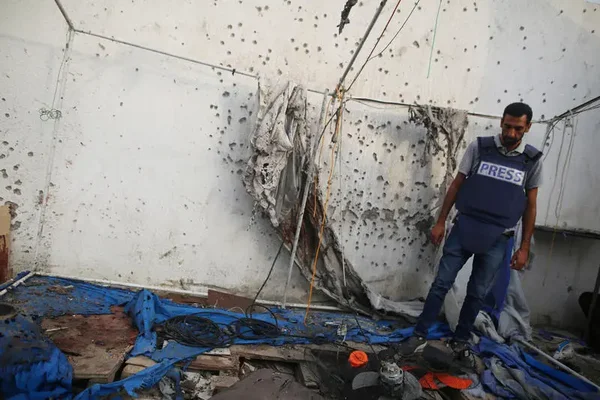 Un journaliste en gilet bleu dans une pièce ravagée par les tirs.