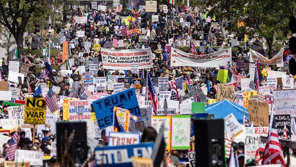 Foule de manifestants avec des drapeaux américains et des pancartes lors d'un rassemblement politique en plein air.