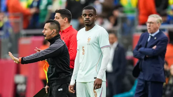 Un international français au bord du terrain lors de Brésil-France, supervisé par un membre du staff.