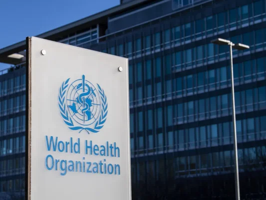 Enseigne de l'Organisation mondiale de la santé (OMS) devant un immeuble moderne sous un ciel dégagé.