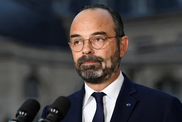 Édouard Philippe en costume bleu marine et barbu, s'exprimant devant des microphones lors d'une déclaration publique.