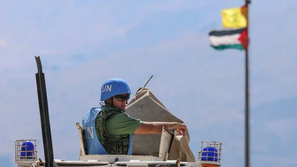 Casque bleu de la FINUL assis sur un véhicule avec un drapeau palestinien en arrière-plan.