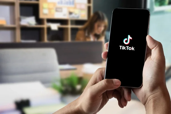 Une personne tenant un smartphone affichant le logo TikTok dans un environnement de bureau