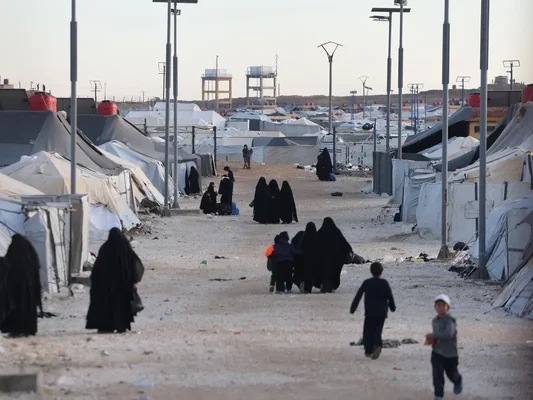 Quatre femmes en vêtements traditionnels marchent sur un chemin de terre près d'une zone clôturée.